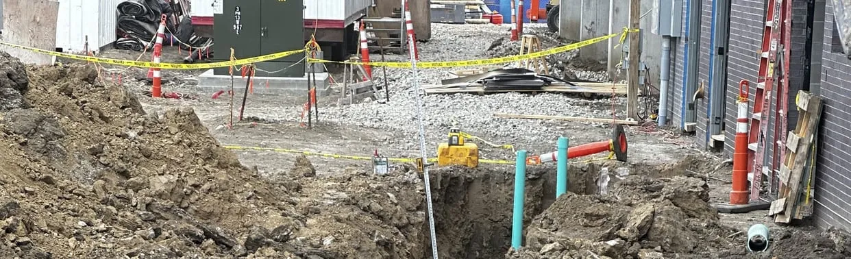Open trench with new sewer pipe on a fenced commercial job site